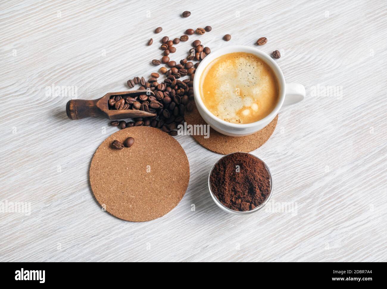 Still life with coffee. Coffee cup, coffee beans, beer coaster and ground powder on light wood