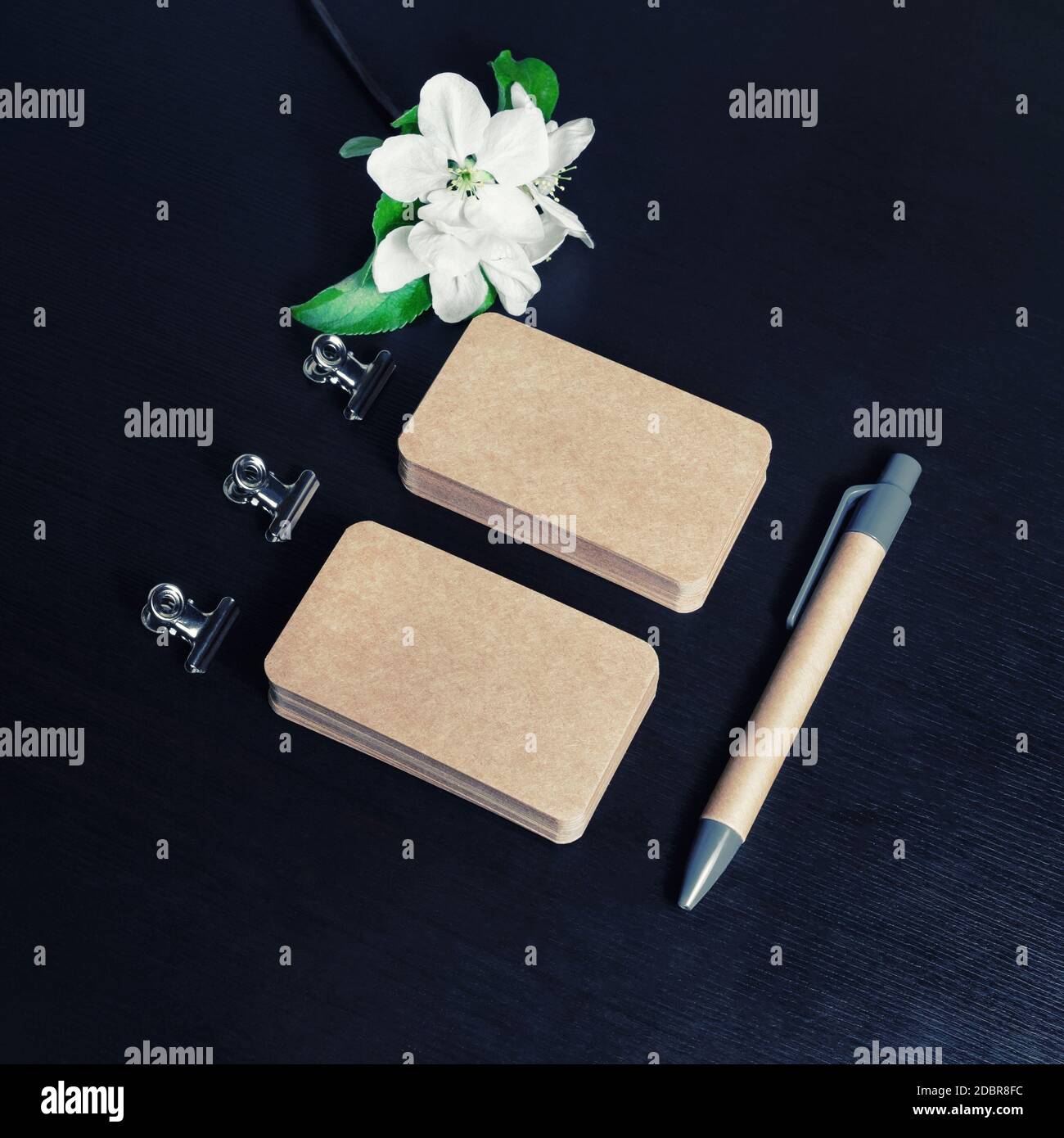 Blank kraft paper business cards, pen and flowers on black wooden
