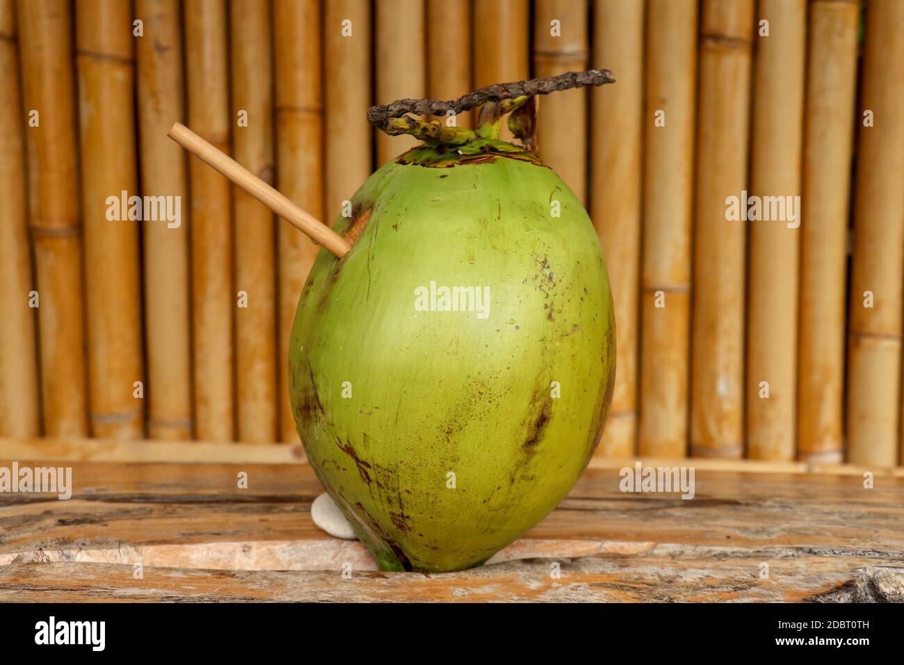 Fresh young coconut with bamboo straw on table with massive wooden ...