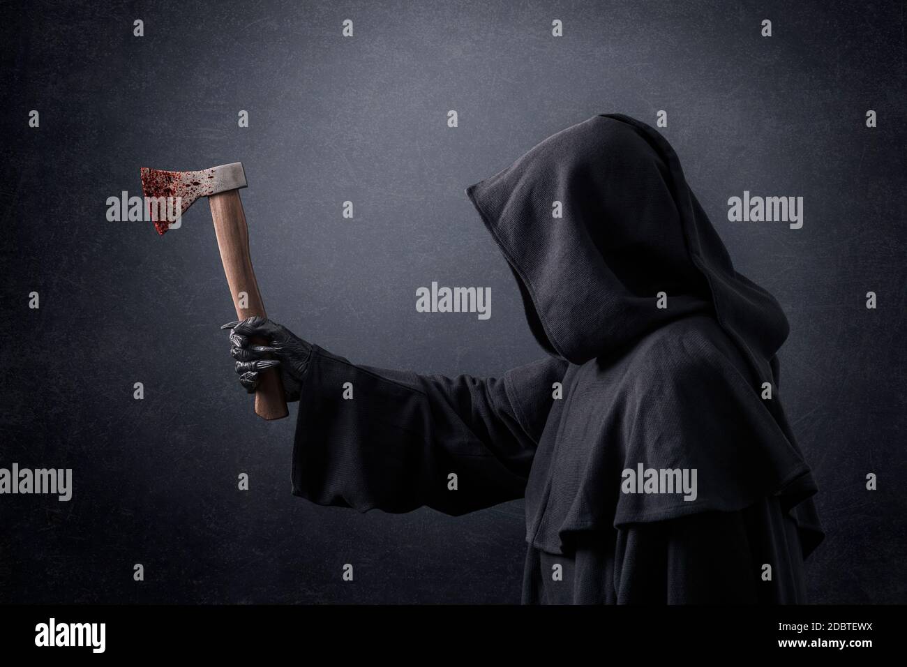 Scary figure in hooded cloak with axe in blood in the dark Stock Photo
