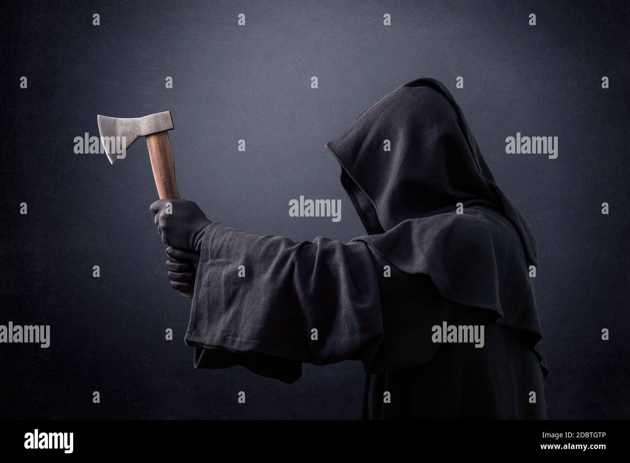 Scary figure in hooded cloak with axe in the dark Stock Photo