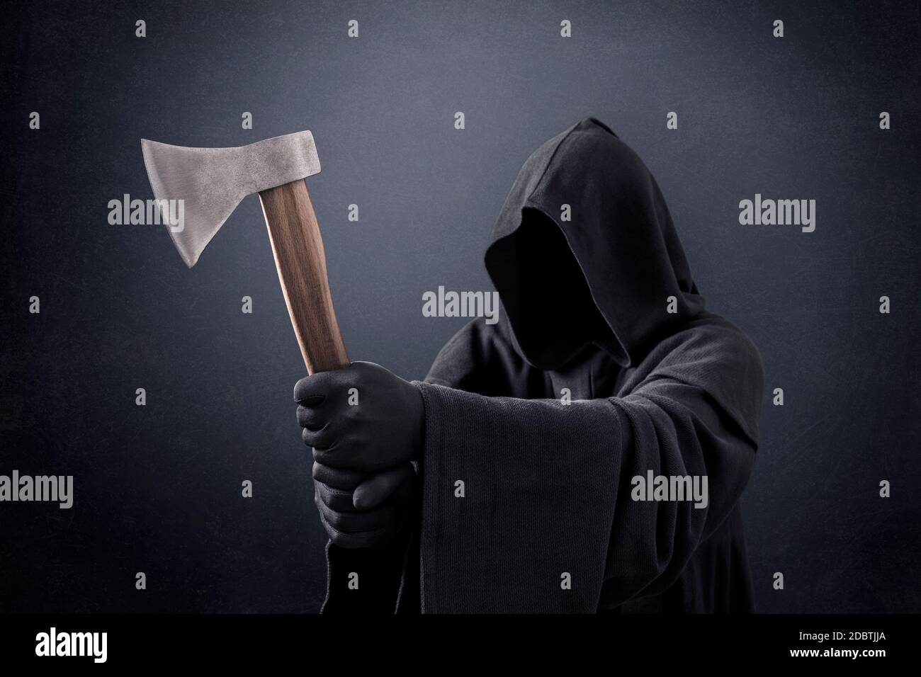 Scary figure in hooded cloak with axe in the dark Stock Photo