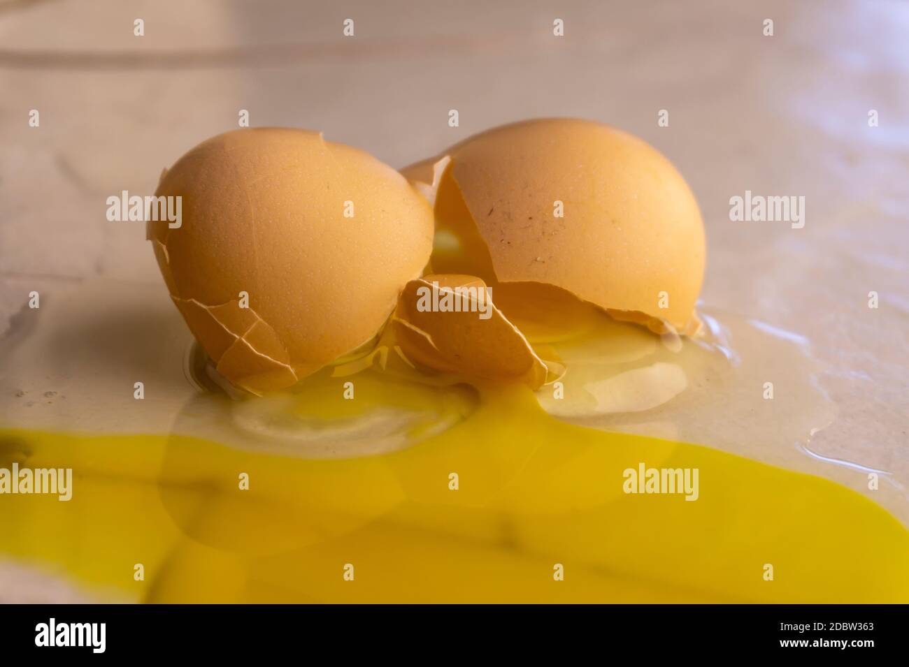 Split yellow yoke and white of a broken egg with the smashed shell on a kitchen counter in close up Stock Photo