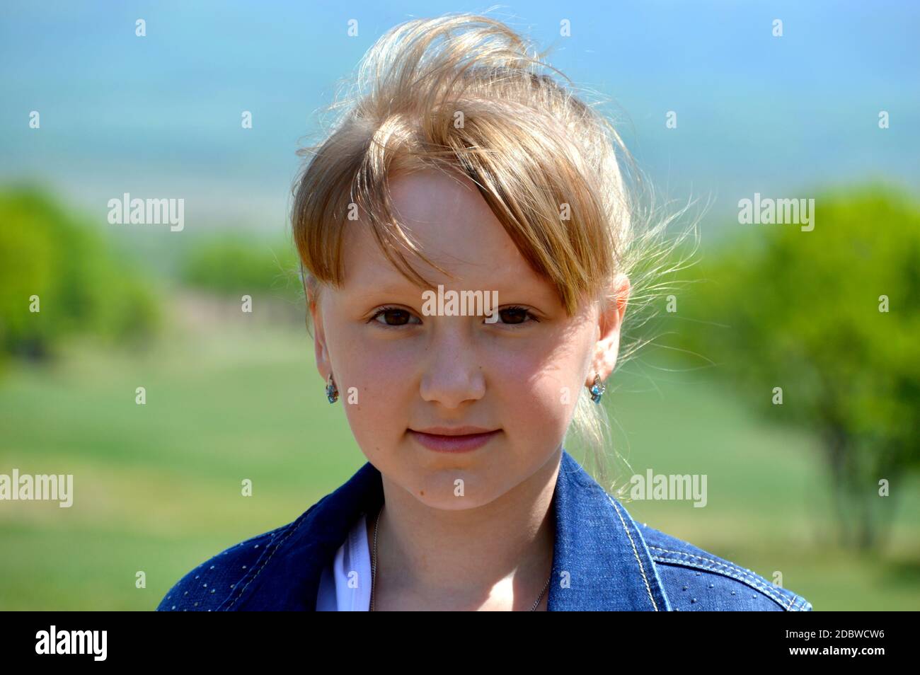 Portrait of 10 year old Russian smiling blonde girl on a background of green field. cute face, looking at the camera Stock Photo