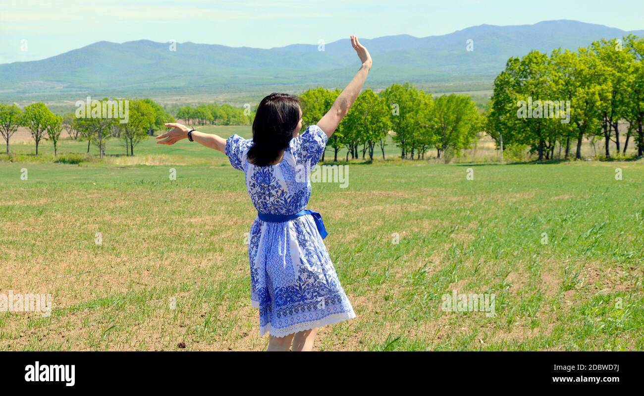 Russian young woman in dress in the Slavic style running and waving her hand to the nature against the background of  green field with trees. summer Stock Photo
