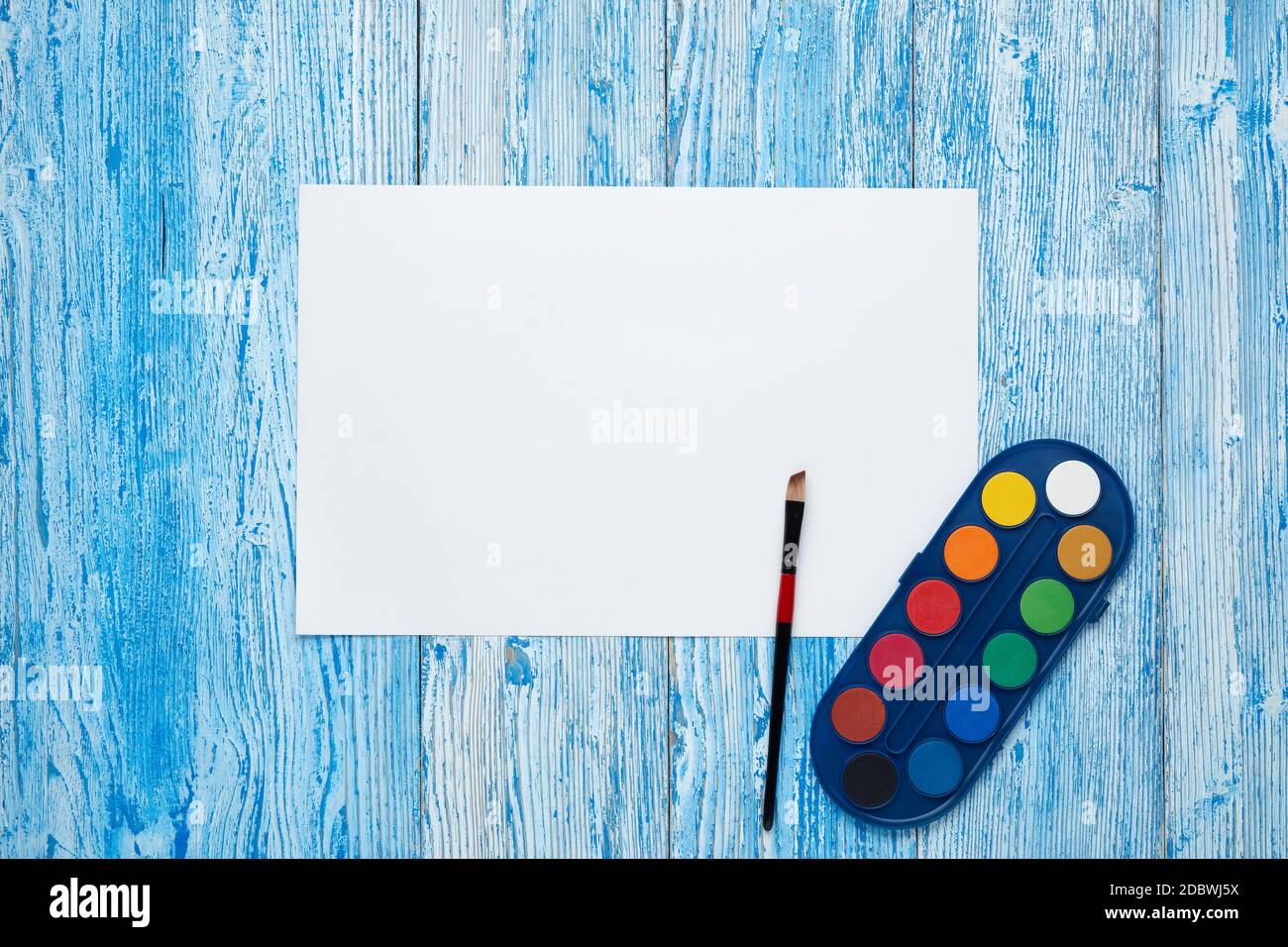 Blank sheet, paints and paint brushe on blue wooden background. Top view, copy space. School accessories for children's education and development. Art Stock Photo