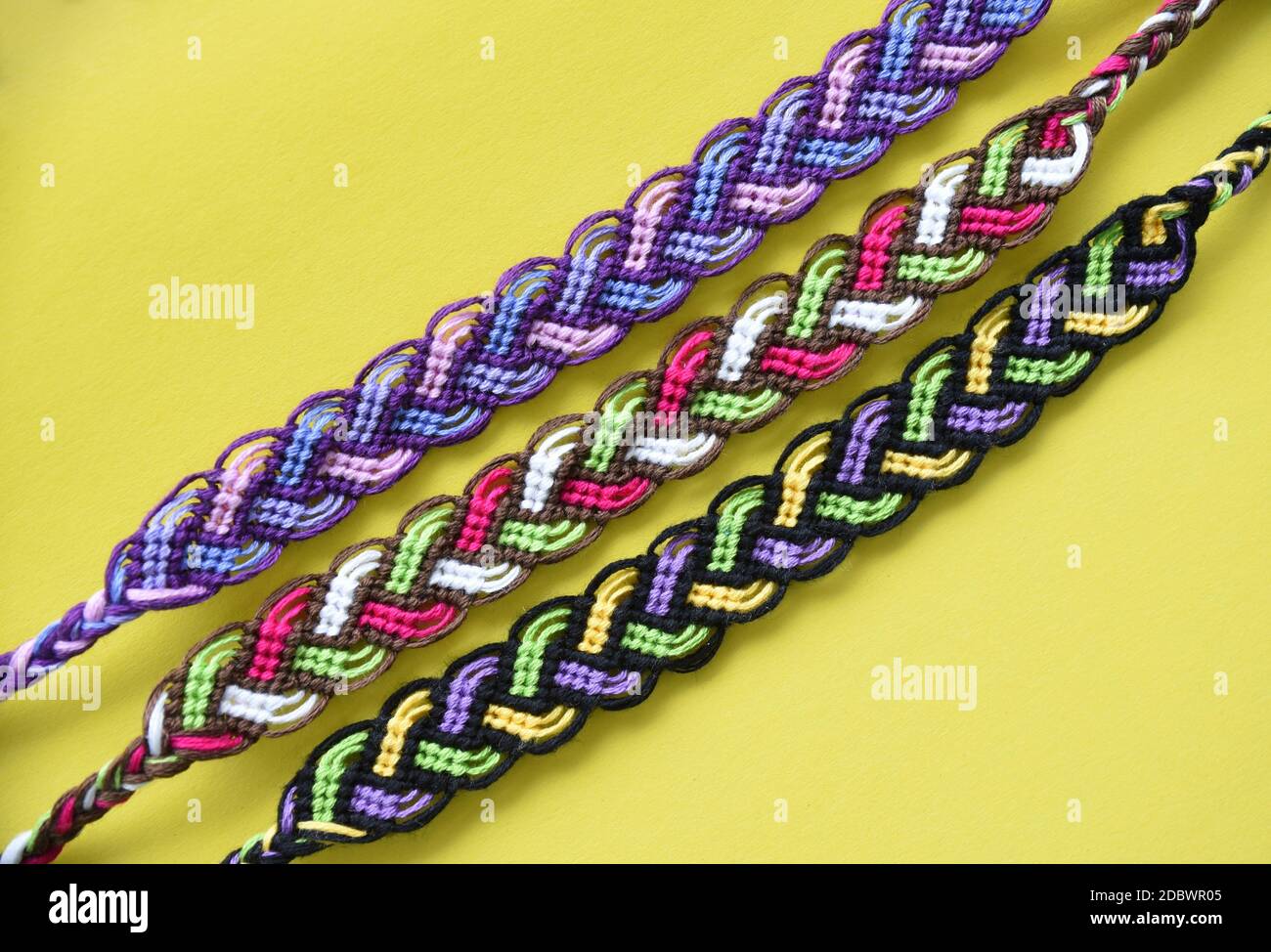 Selective focus of multi-colored woven DIY friendship bracelets Pigtail handmade of embroidery bright thread with knots on yellow background Stock Photo