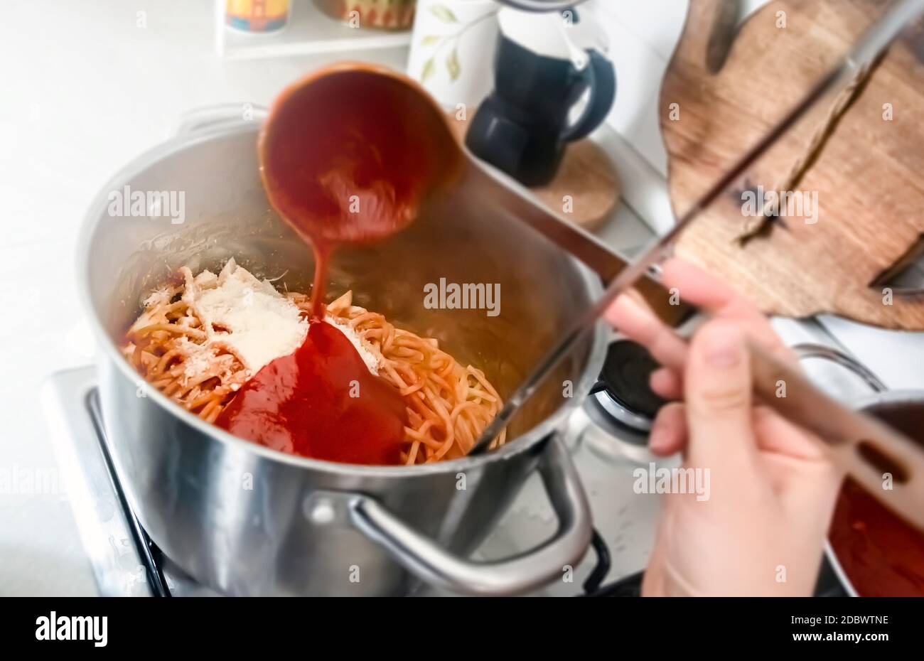 Seasoning a pan full of freshly cooked spaghetti by pouring the tomato sauce with a steel ladle. Italian home cooking. Stock Photo