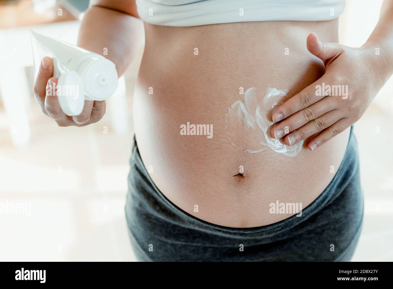 Happy pregnant woman apply skincare cream lotion on pregnant belly to