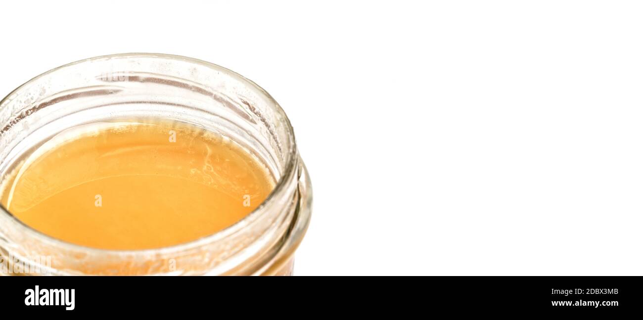 Glass jar with amber colored honey, closeup detail, isolated on white background, space for text right side. Stock Photo