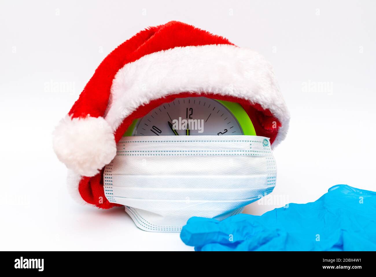 New Year alarm clock santa hat medical mask rubber gloves on white background countdown to midnight.Clock showing nearly 12. Stock Photo