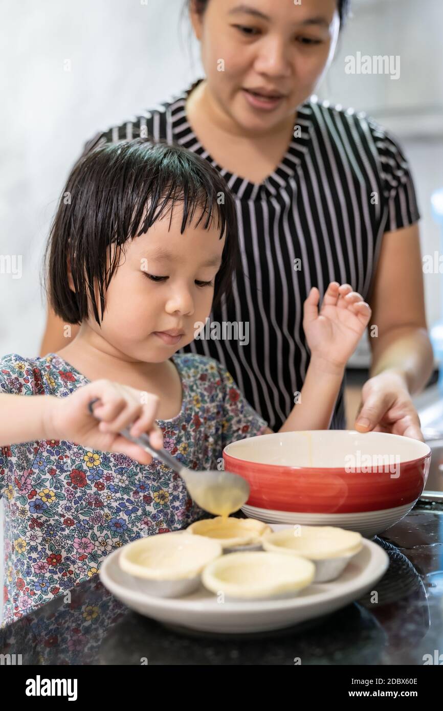 Asian girl cooking egg tart bakery with her mom, housework for child make executive function for kid. House-working food lifestyle and family concept. Stock Photo
