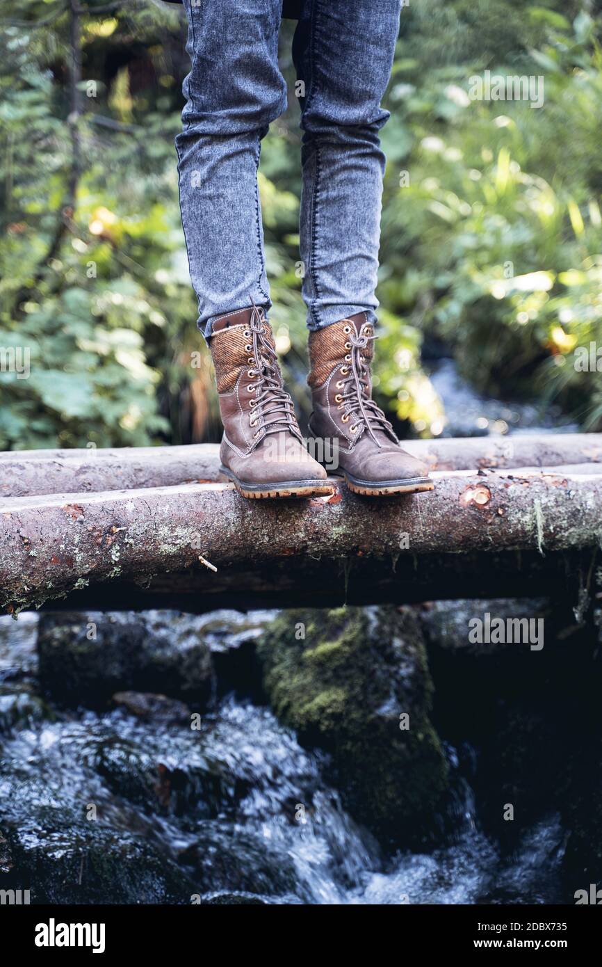 front view closeup of woman with brown tall leather hiking boots and grey  jeans standing on a wooden trunk tree bridge over a mountain water stream  in Stock Photo - Alamy
