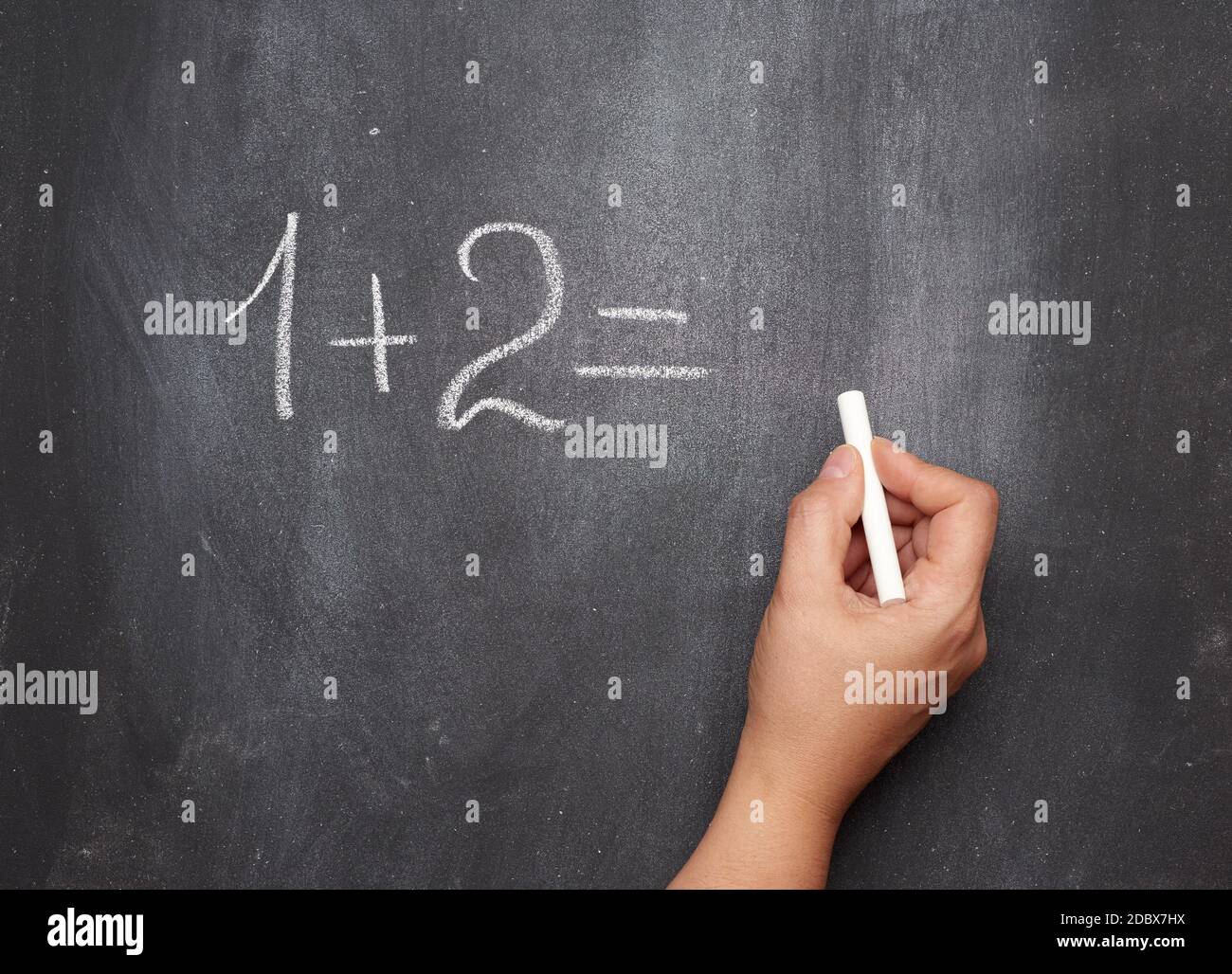 math example written in white chalk on a black chalk board and a woman's hand with white chalk, one plus two Stock Photo