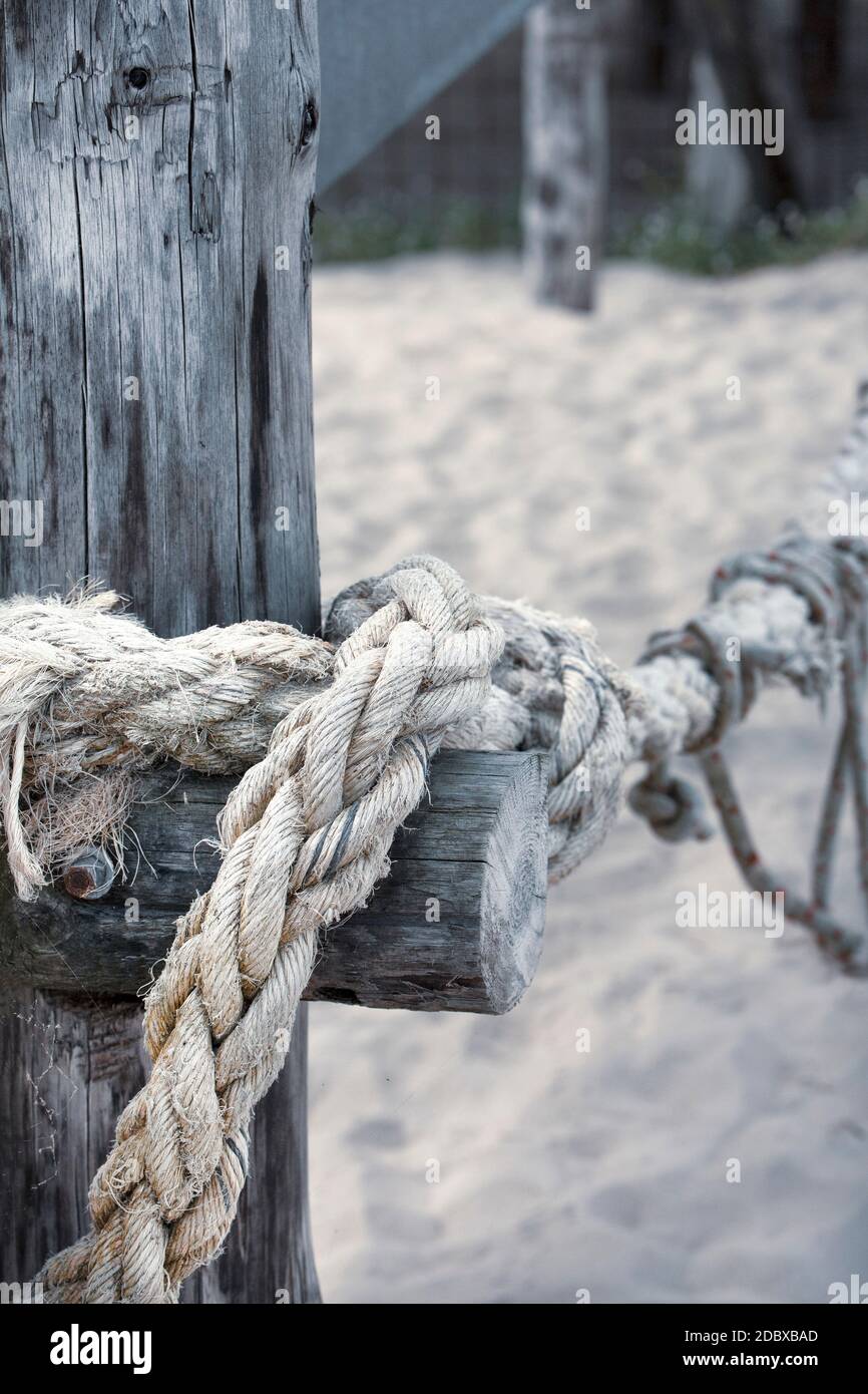 massive ship rope tied around a weathered wooden post from a jetty