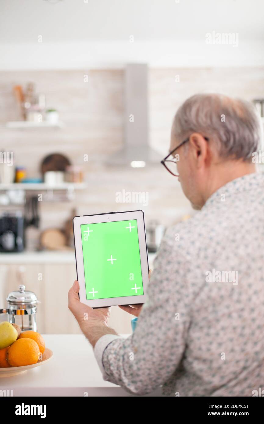 Mature man holding tablet pc with chroma key in kitchen during breakfast. Elderly person with green screen isolated mock-up mockup for easy replacement Stock Photo