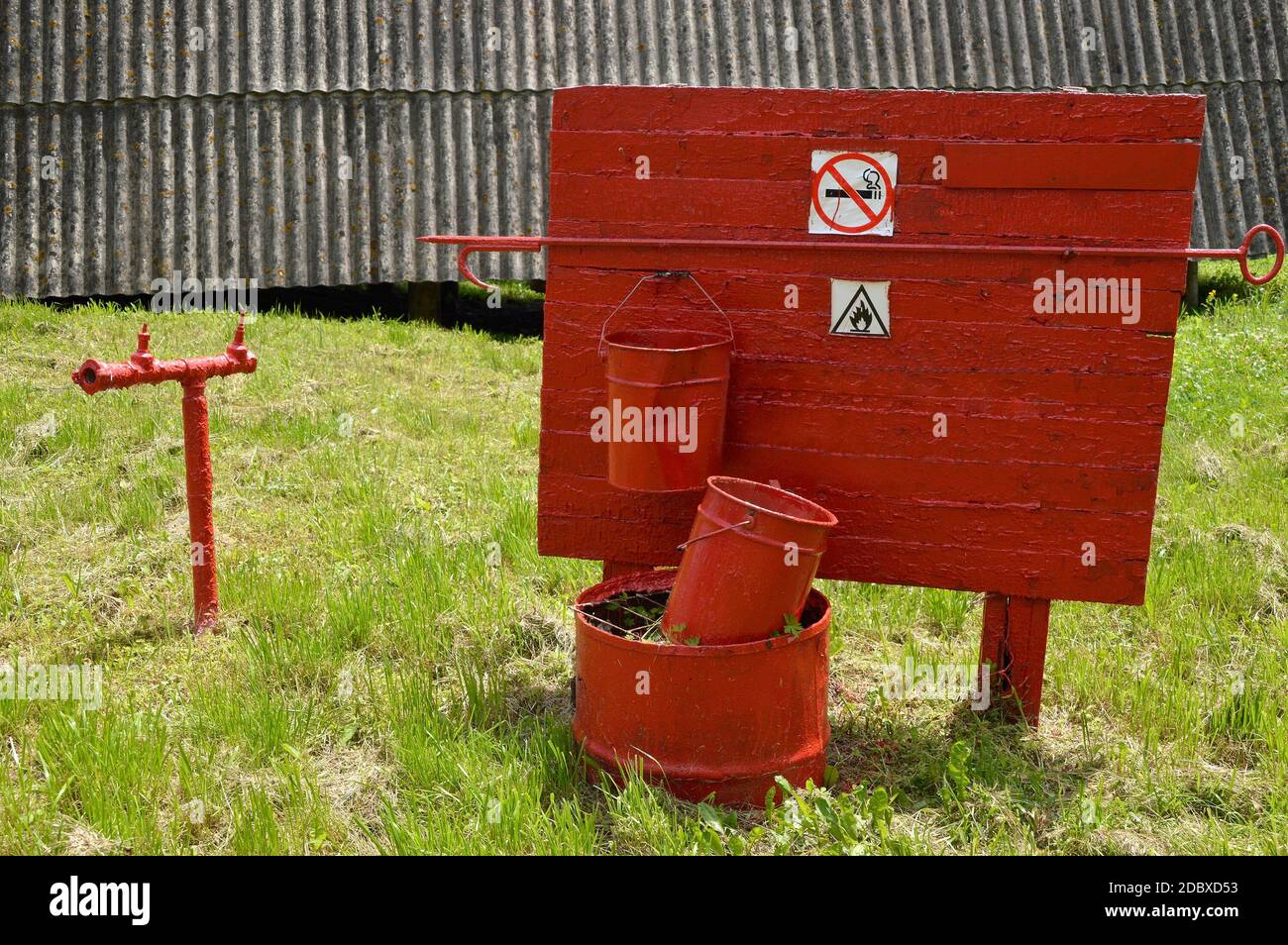 Fire extinguishing equipment. Hydrant stand pipe and two buckets hanging on the board. Shabby and old with rusty red paint Stock Photo