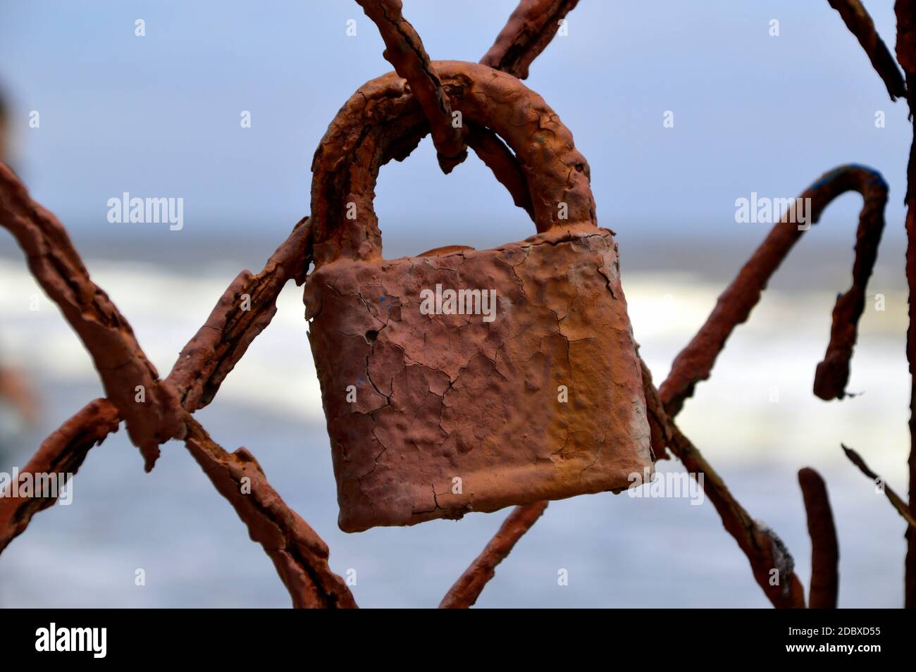 Old ferruginous padlock hanging on a rusty fence on a sea background Stock Photo