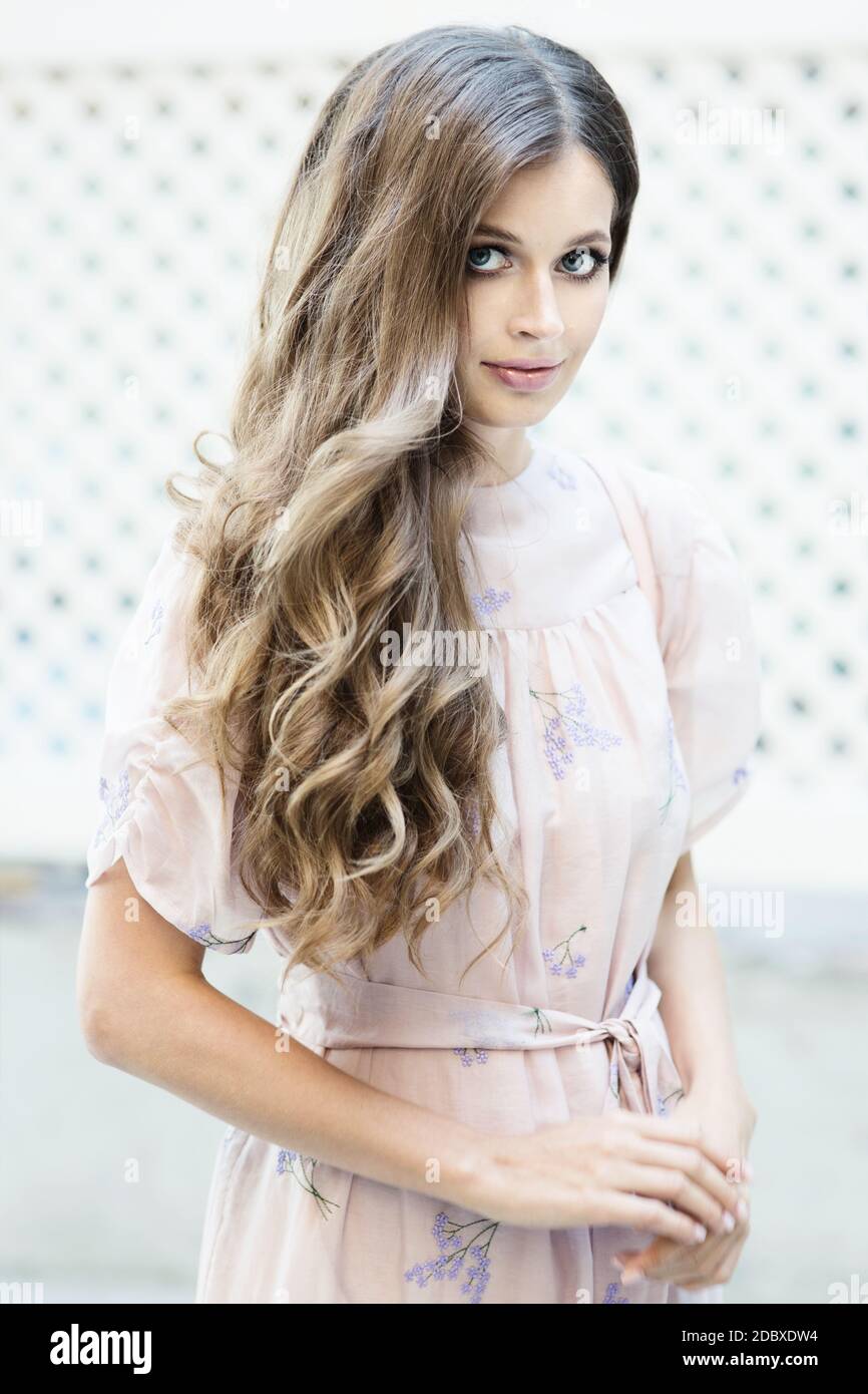 Portrait of a beautiful long-haired girl in a fashionable pink dress stands and smiles on the city street Stock Photo