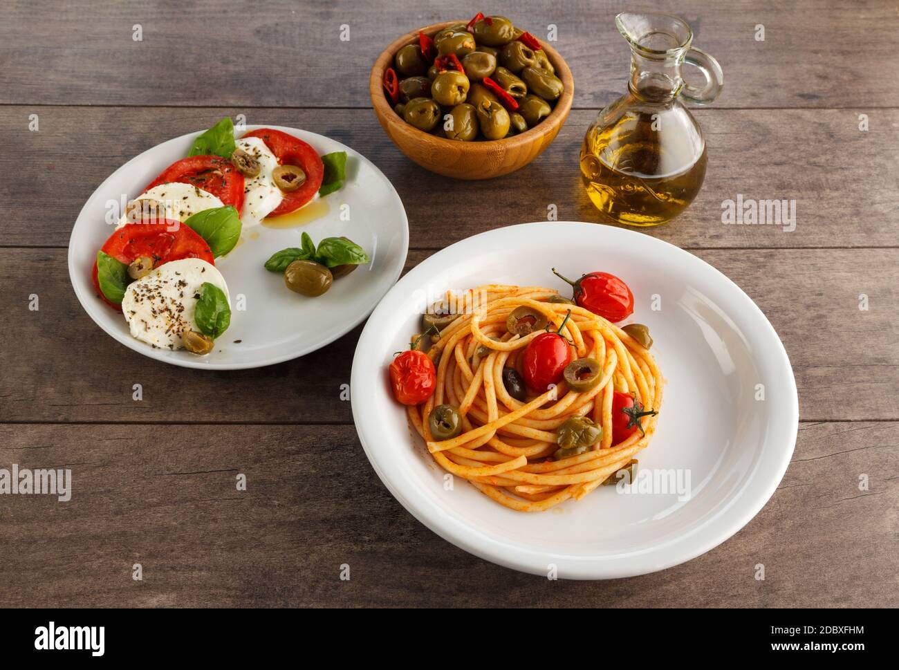 Full table of italian meals on plates. Spaghetti, caprese, olives and