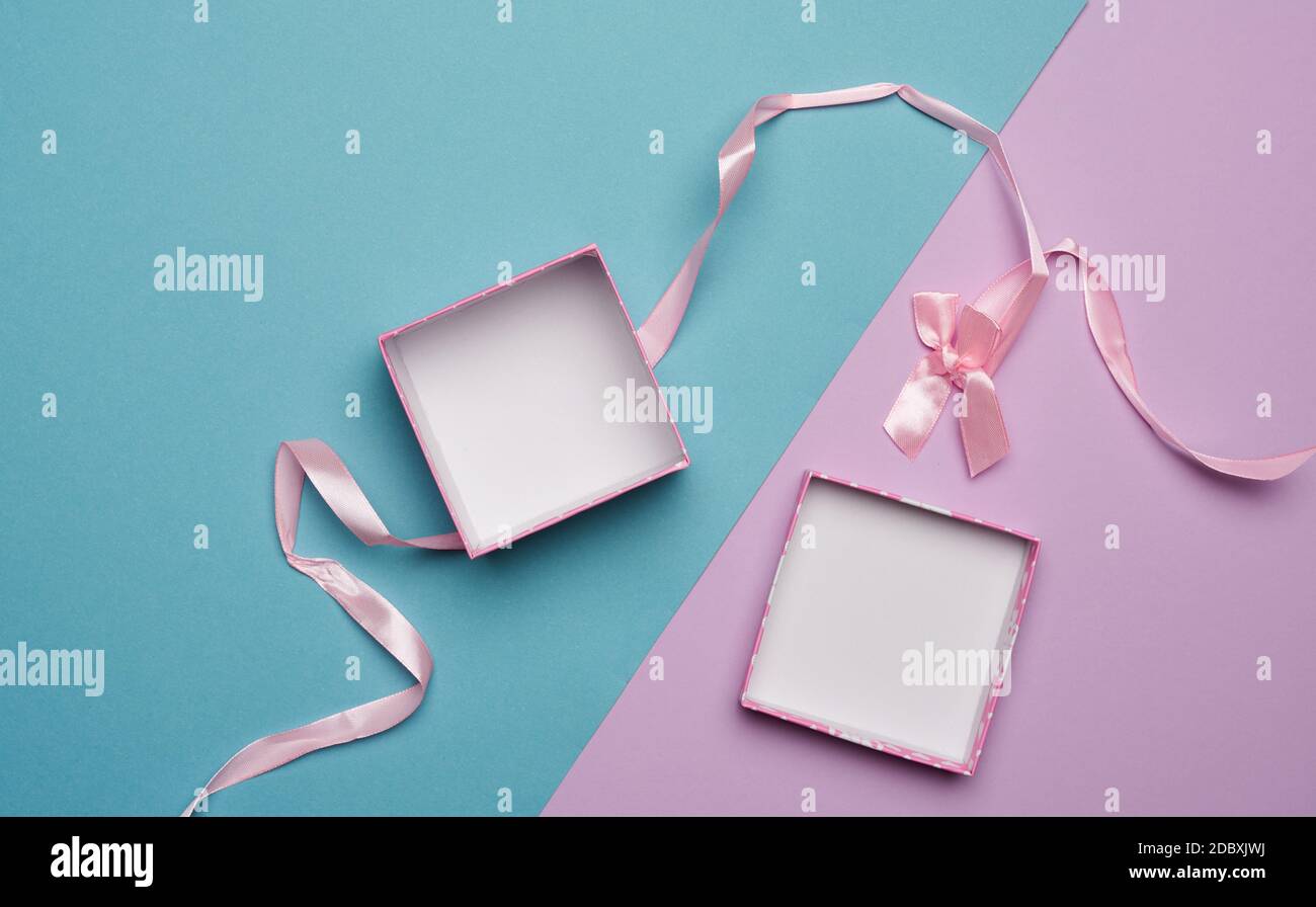 empty open cardboard box and pink ribbon with bow on blue lilac background, flat lay Stock Photo