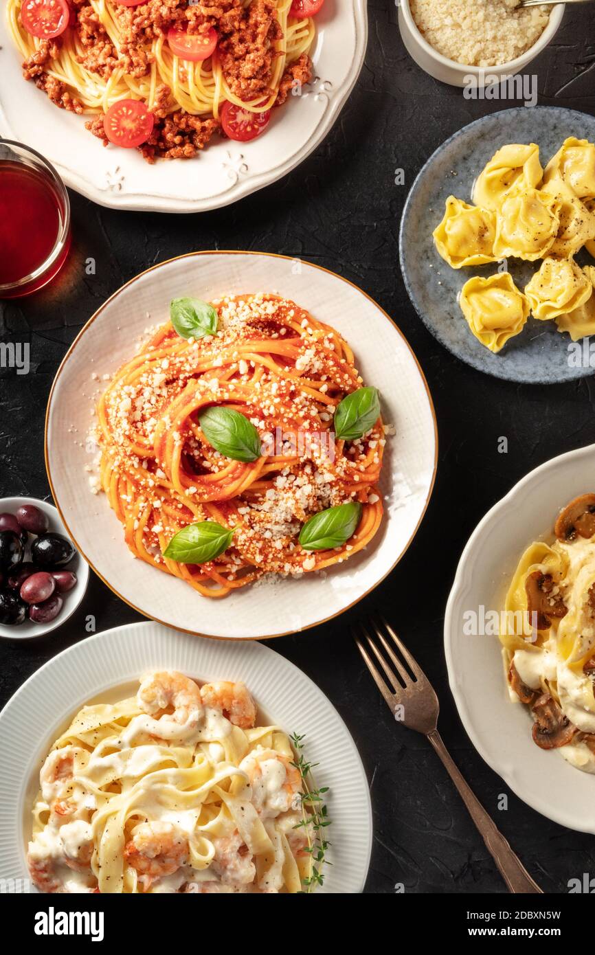 Pasta dishes variety. Pastas with meat, vegetables, seafood and mushrooms, with ravioli, grated Parmesan cheese, and wine, top shot Stock Photo