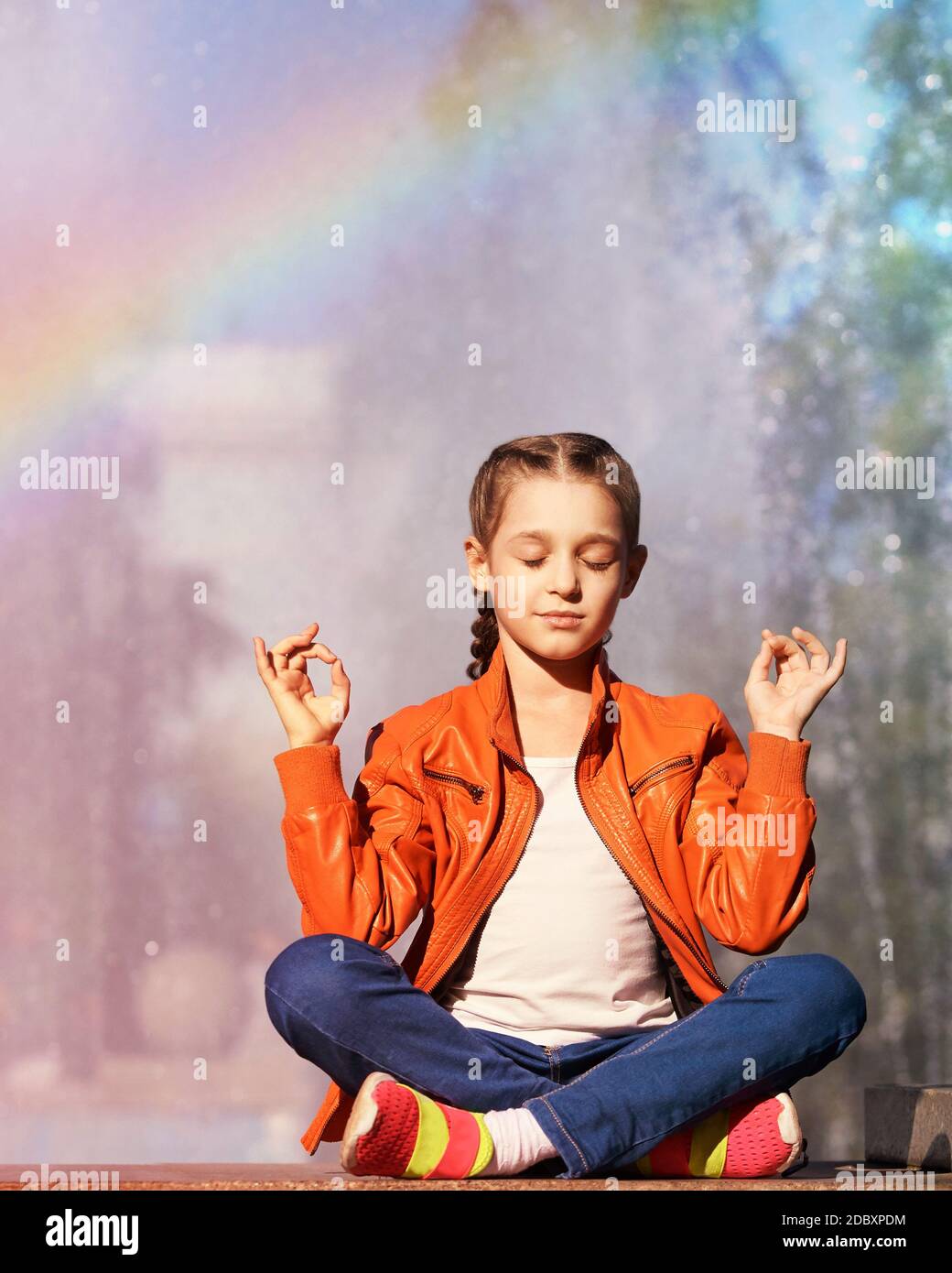 Little girl in bright orange clothes sitting in yoga pose Stock Photo