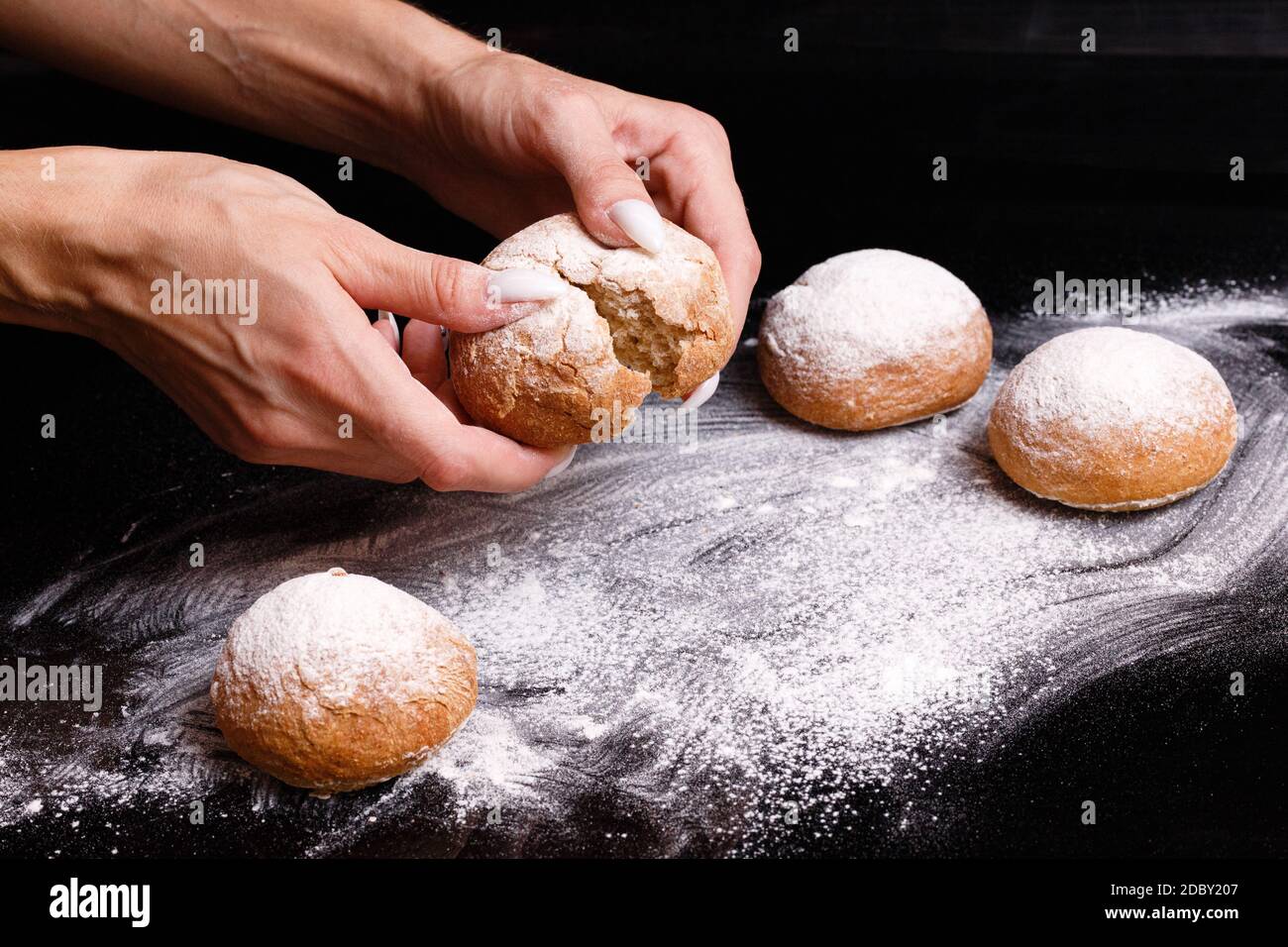 Homemade pastries. White buns are separated by hand. Photo of baking on a black background. Donuts sprinkled with powder. Stock Photo