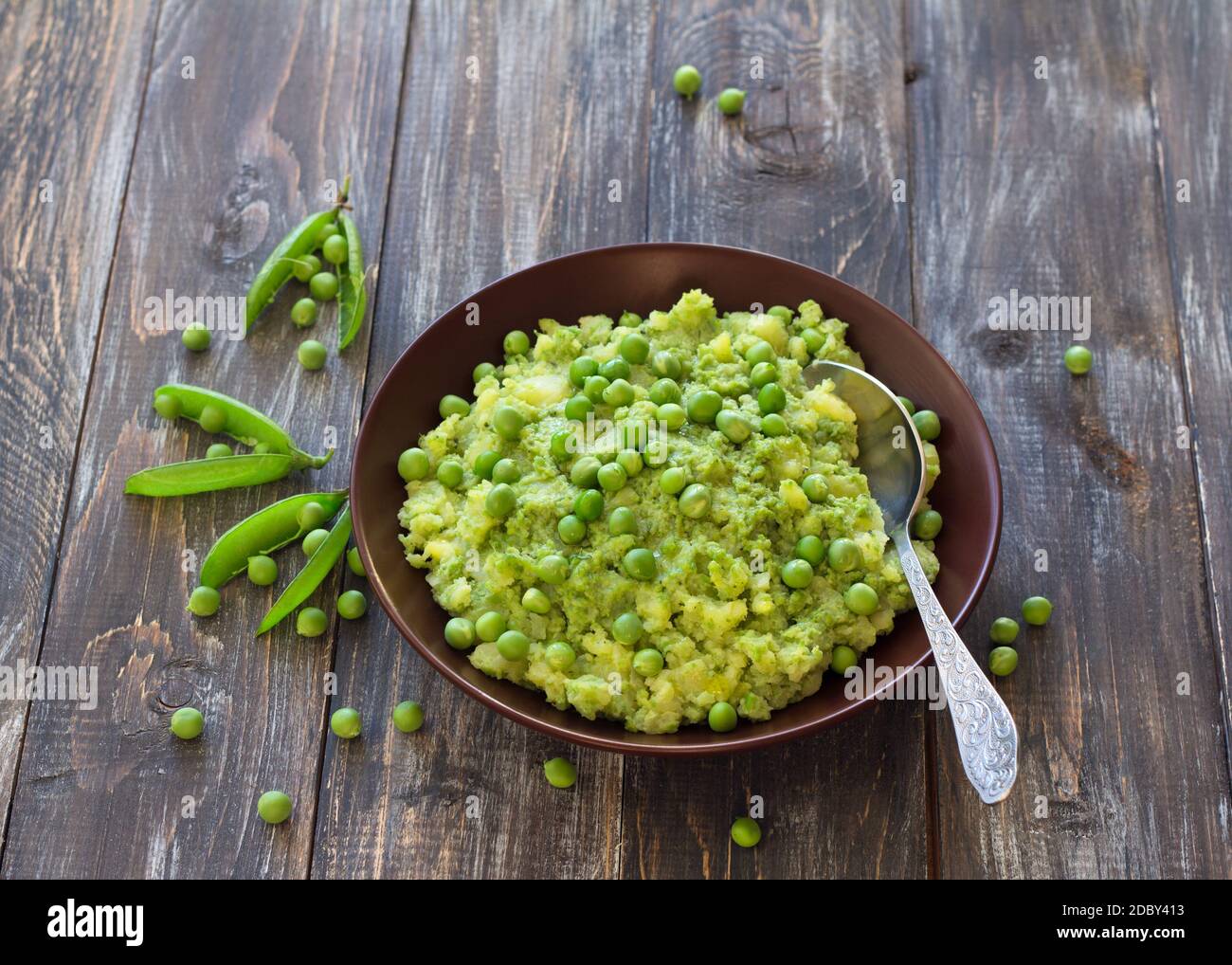 Mashed potatoes with green peas and olive oil in a ceramic bowl on a wooden table. Healthy vegetarian food Stock Photo