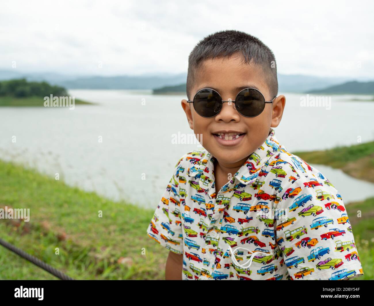 An Asian boy sitting and wearing glasses On the background of the reservoir at the tourist attractions in Thailand. Stock Photo