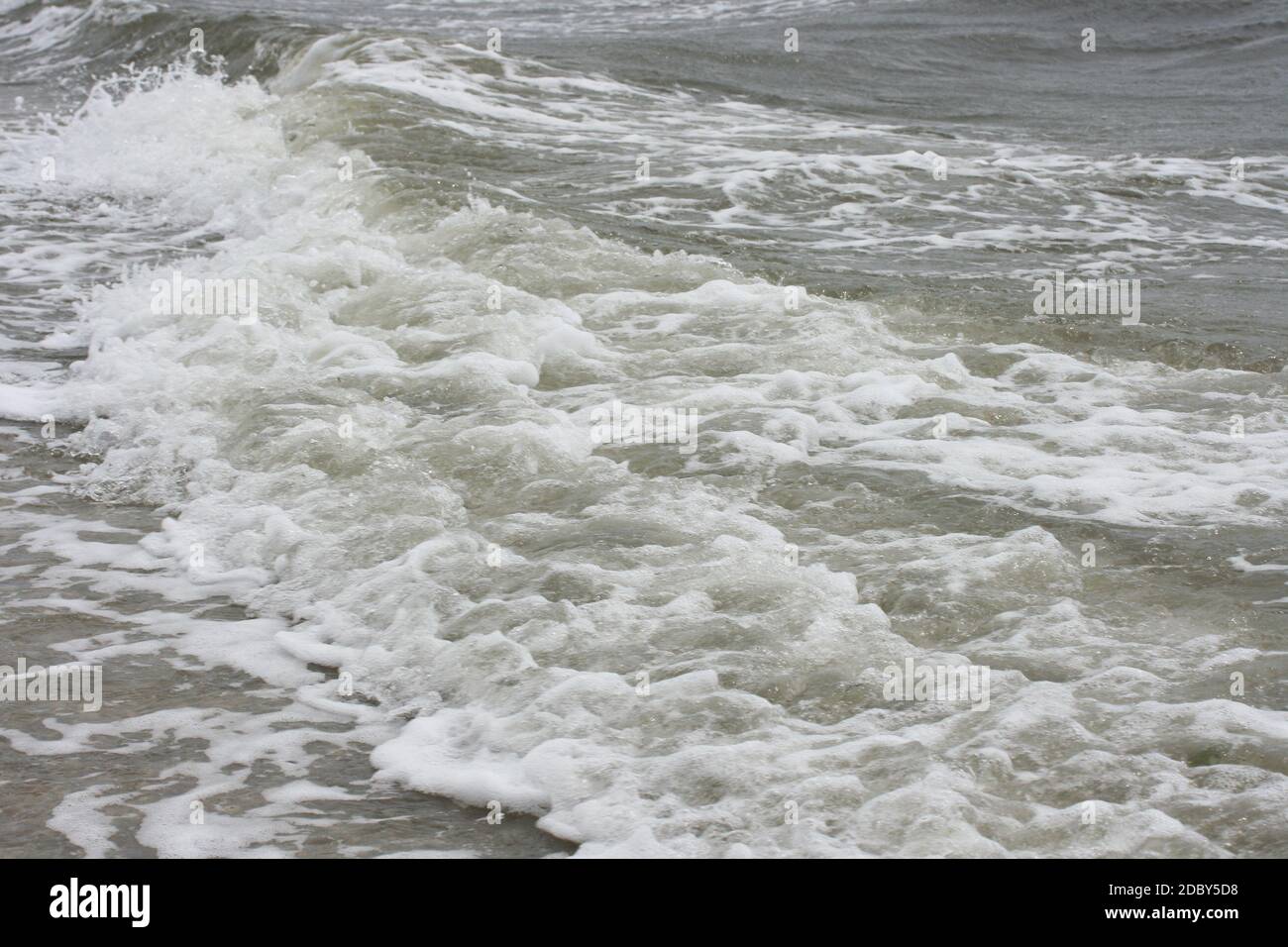 Waves with white crests inundate the sandy beach Stock Photo