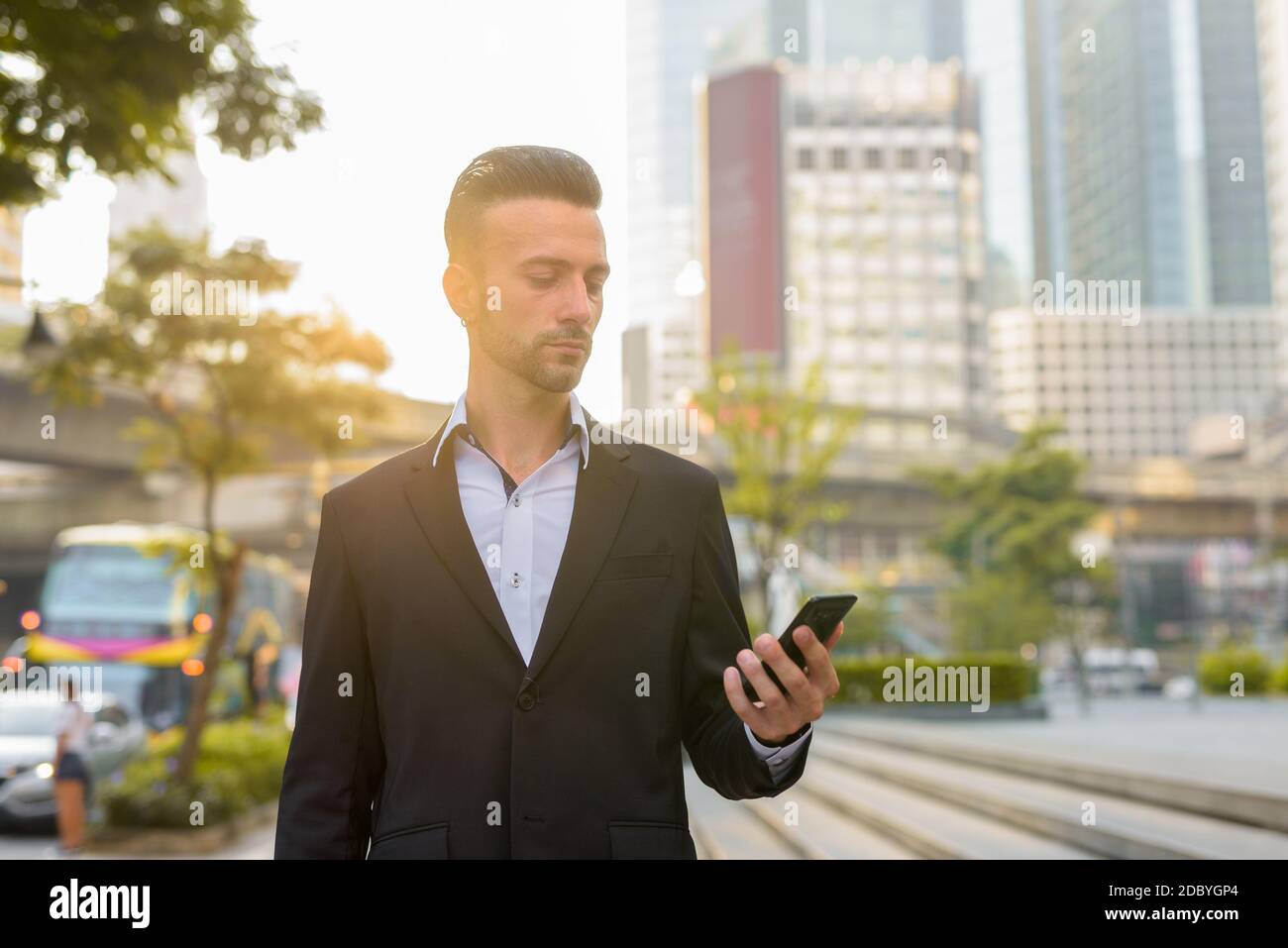 Portrait of handsome young businessman outdoors in city using phone Stock Photo