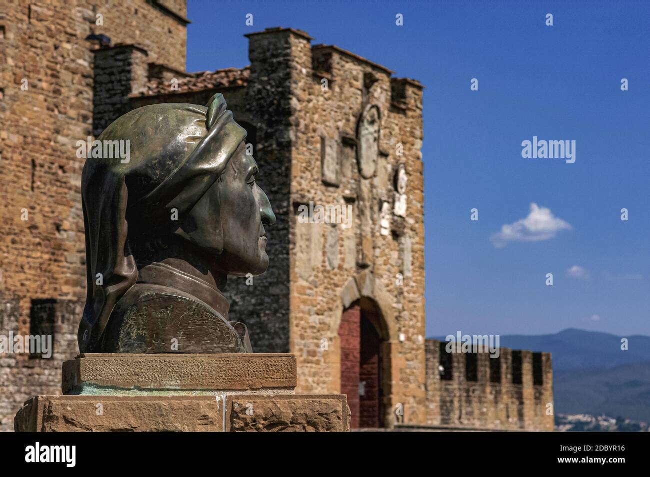 Bronze bust of Italian poet Dante Alighieri (c. 1265-1321) by the Munition Tower, or Antiporta della Munizione, of the medieval Castle of the Guidi Counts, or Castello dei Conti Guidi, at Poppi, Tuscany, Italy.  Dante fought at the nearby Battle of Campaldino for the victorious Florentines in 1289.  Poppi castle was built around 1274.  The Munition Tower (in the background) was added as an outer defence in the 1400s. Stock Photo