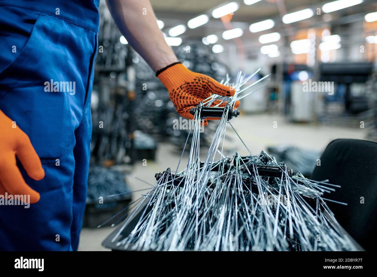Worker in uniform shows new bicycle spokes on factory. Bike wheels assembly in cycle