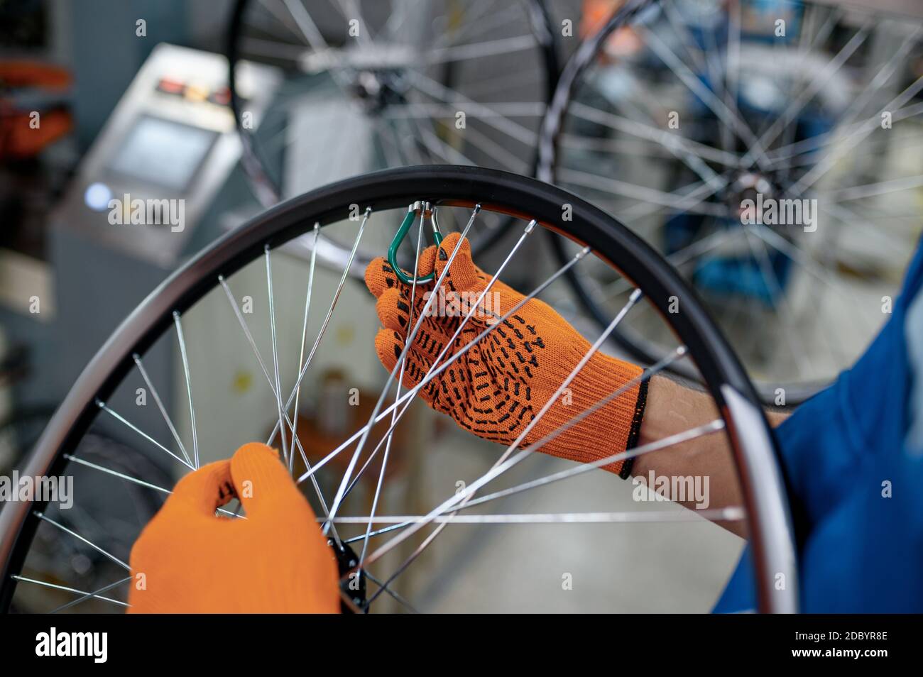 Worker in gloves installs new bicycle spokes on factory. Bike wheels