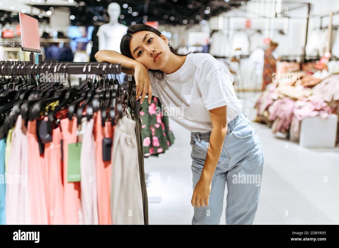 Woman shopping clothes. Female shopper looking at fashionable clothes  indoors in clothing store. Stock Photo