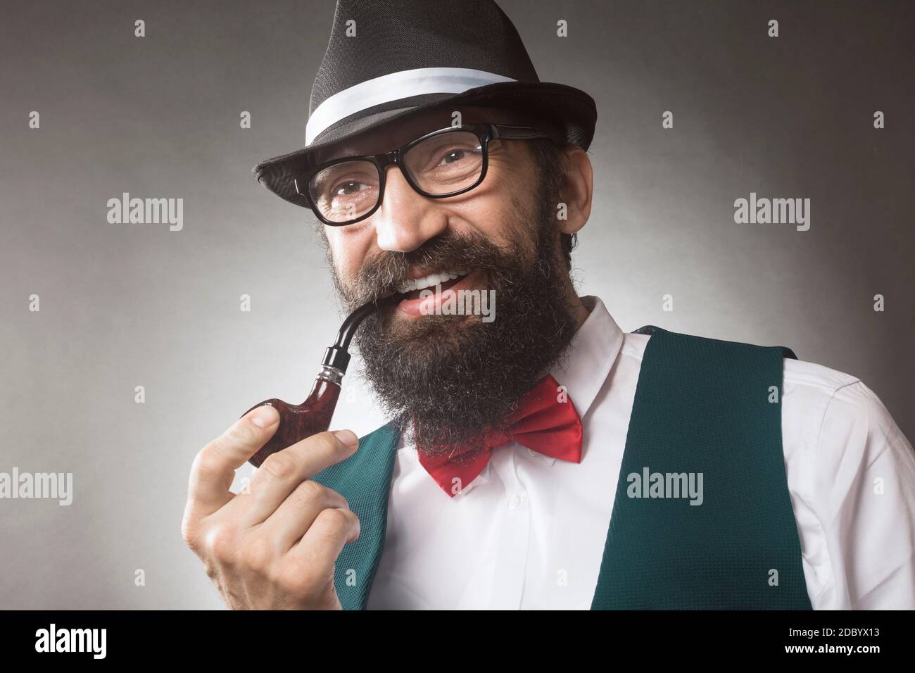 The smiling elegant bearded man is smoking tobacco pipe, middle aged man studio portrait. Stock Photo