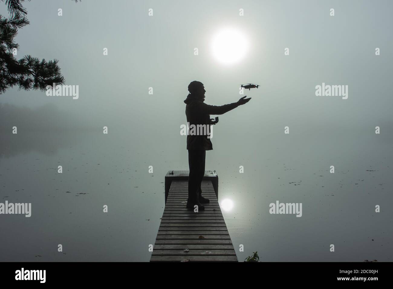 Man playing with the drone. Silhouette against the foggy landscape.Male operating the drone by remote control and having fun. Pilot flying drone. Use Stock Photo