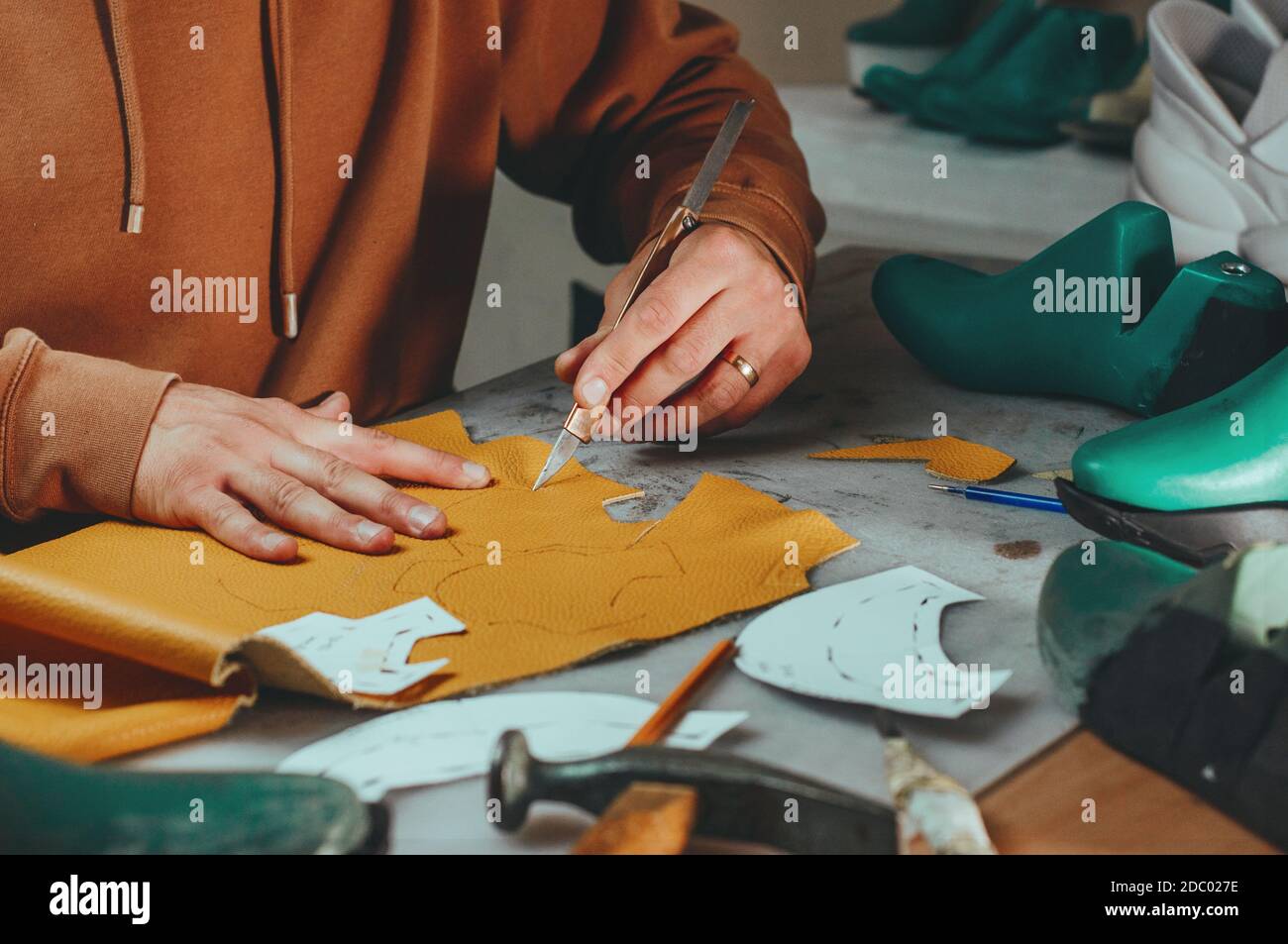 Shoemaker cutting patterns using knife from leather in his workshop. Stock Photo