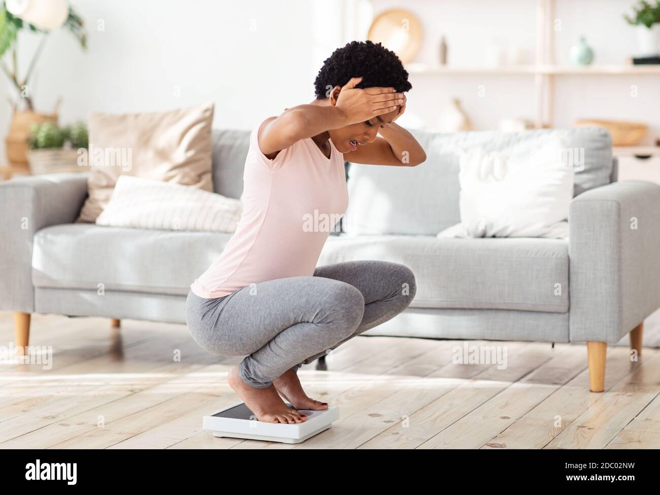 Young black woman sitting on scales, shocked over weight gain at home, free space Stock Photo