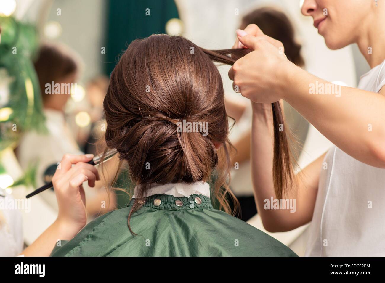 Makeup artist and hairdresser are preparing hairstyle and visage of young woman in beauty salon