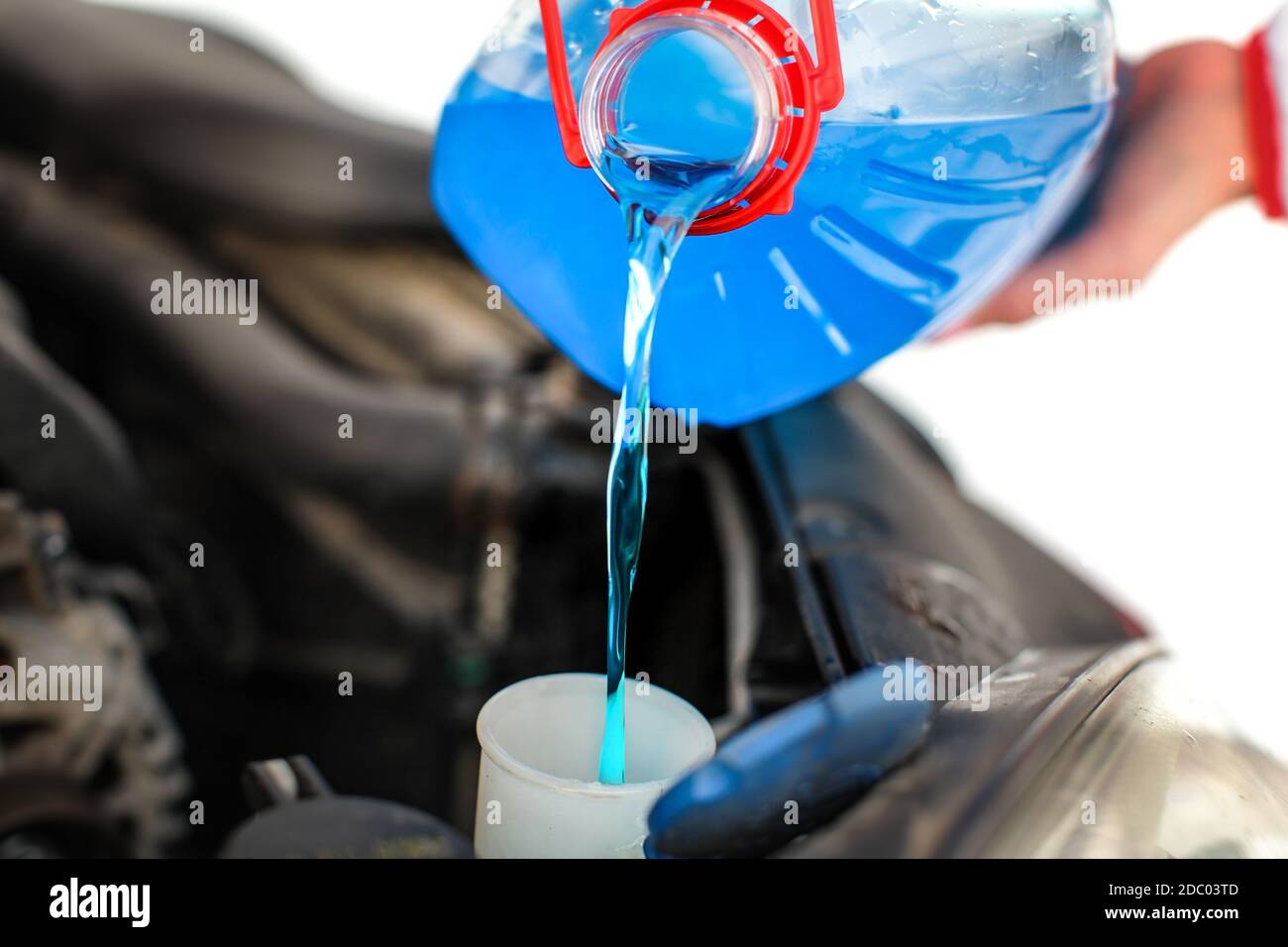 Woman pouring blue antifreeze liquid into dirty car. Stock Photo