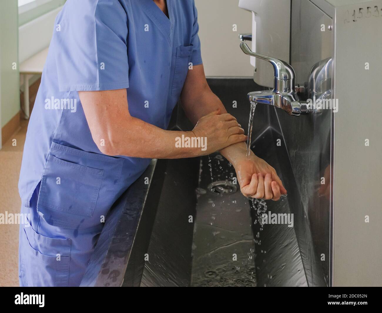 A surgeon washes his hands under a faucet in a stainless steel wash
