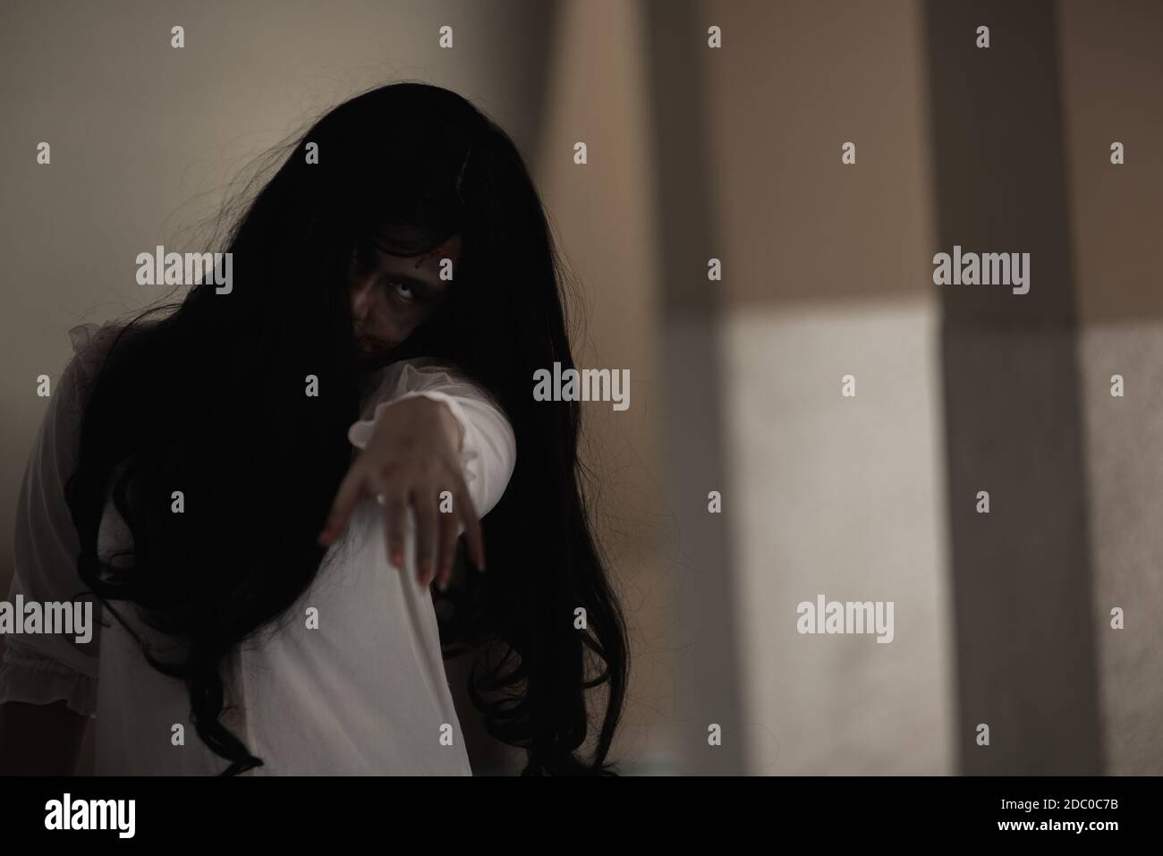 Girl zombie in blood. Asian Woman ghost with blood. Horror scary fear in house dark tone raise hand and reach out. Closeup hair covering the face her Stock Photo
