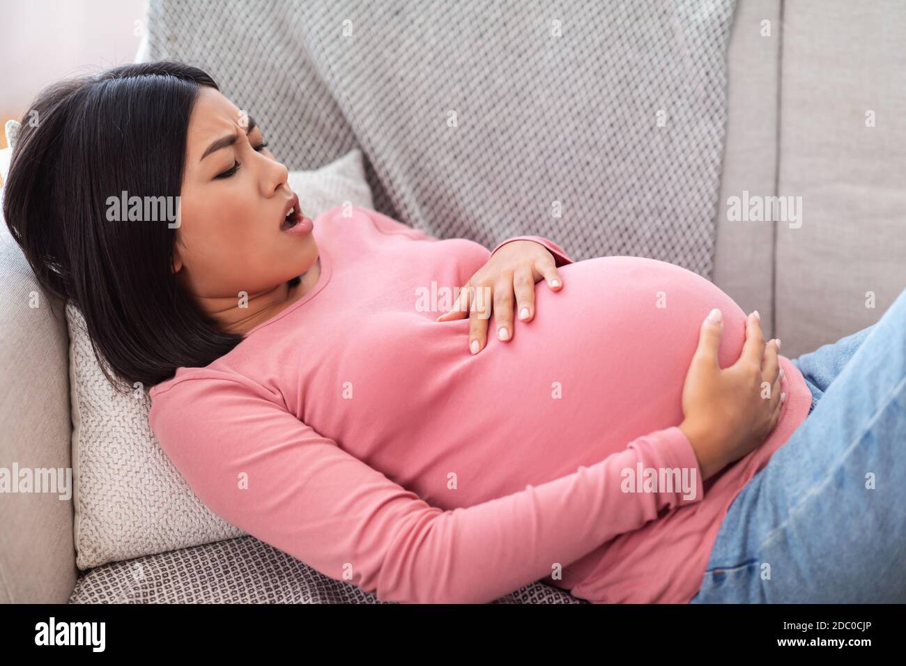 Pregnant Asian Woman Touching Belly Having Painful Contractions At Home Stock Photo