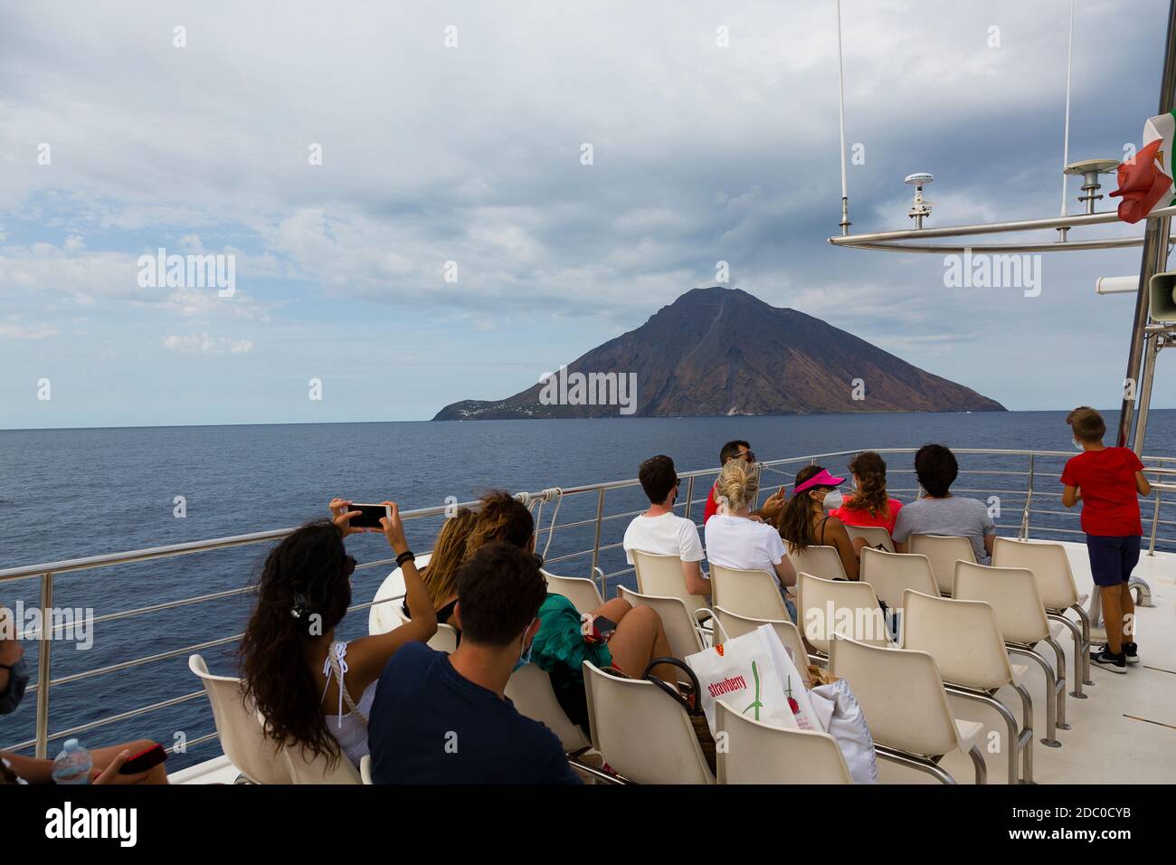 Sicily, Italy. Tourists on the deck of a sightseeing boat watch and take pictures of a plume of smoke rising from the active volcano of Stromboli. Stock Photo