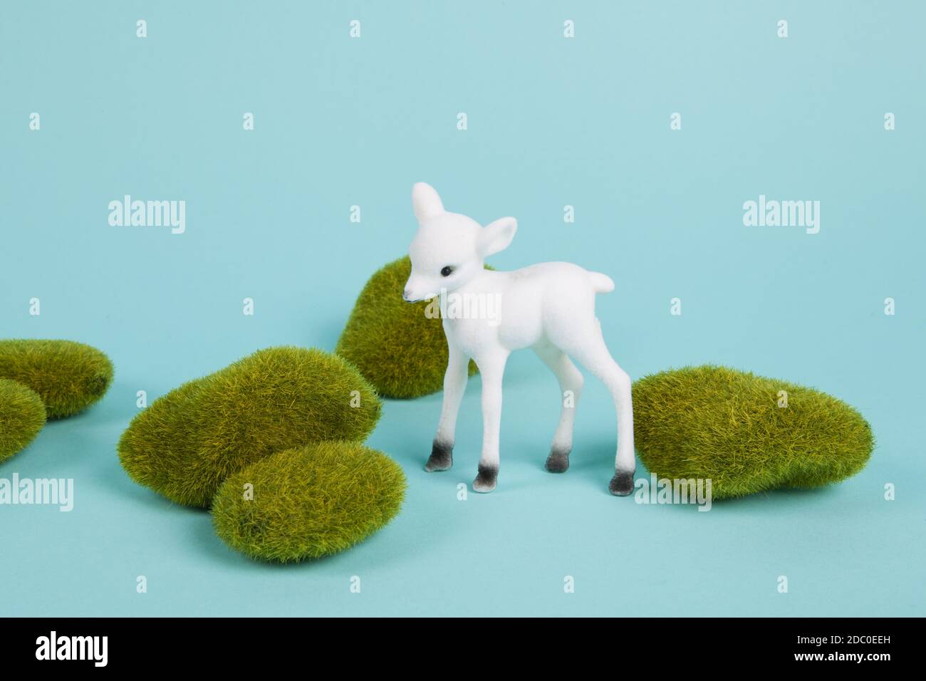 a white fawn among moss rocks set on a blue background. Pop atmosphere. minimal color still life photography Stock Photo