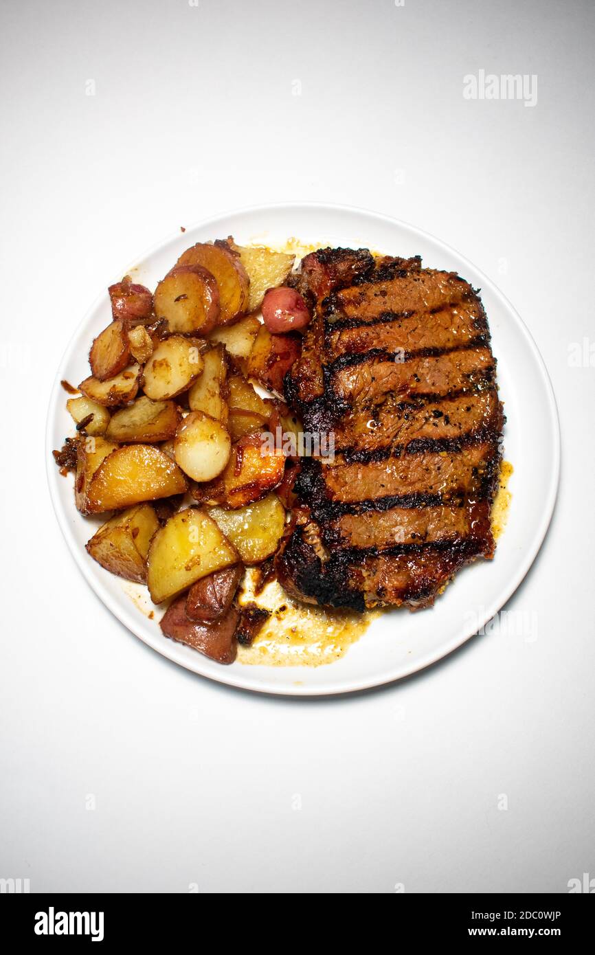 A Perfectly Grilled Steak With Black Grill Lines and Potatoes Plated on a Pure White Background