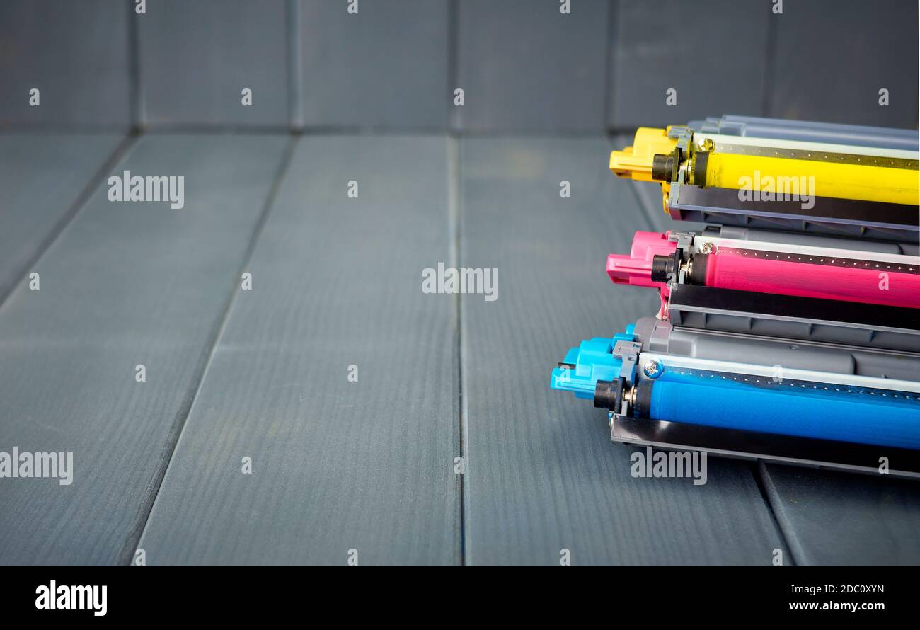 Three used toner cartridges in a color laser printer stacked on gray wooden background for
