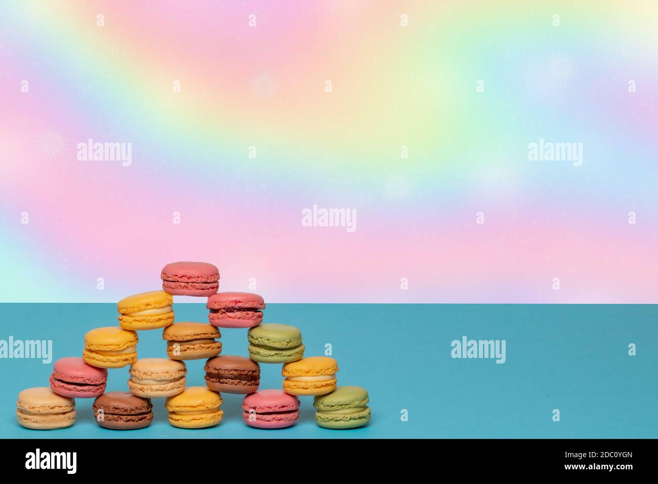 Macaron pyramids. Close-up of colourful French macaroons in shape of a pyramid on a blue table against abstract bright pastel colored background. Adve Stock Photo